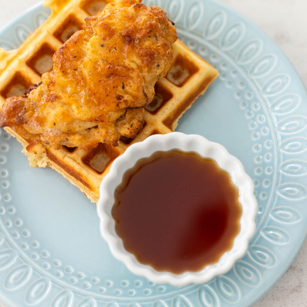 A white dip cup is filled with seasoned maple syrup for chicken and waffles.
