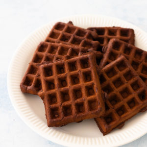 A white plate has a pile of freshly griddled chocolate belgian waffles.