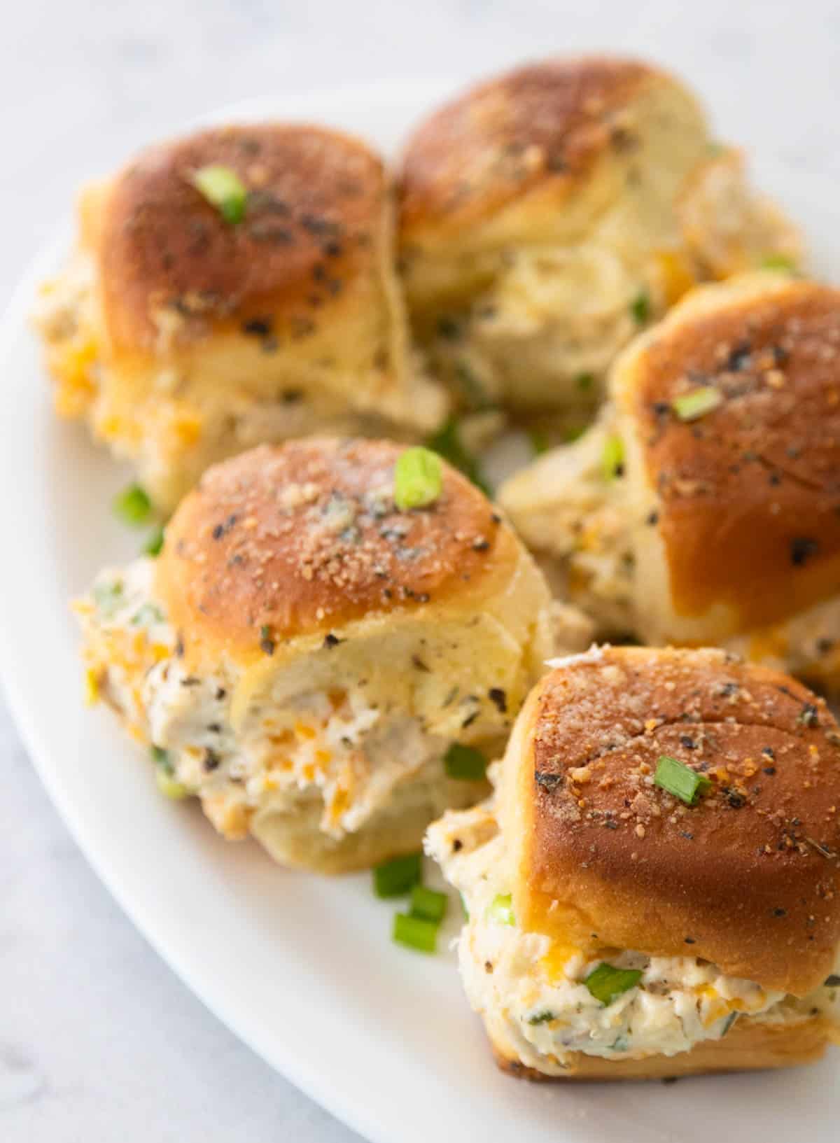 The baked crack chicken sliders are on a white serving platter. Green onions have been sprinkled over the top.