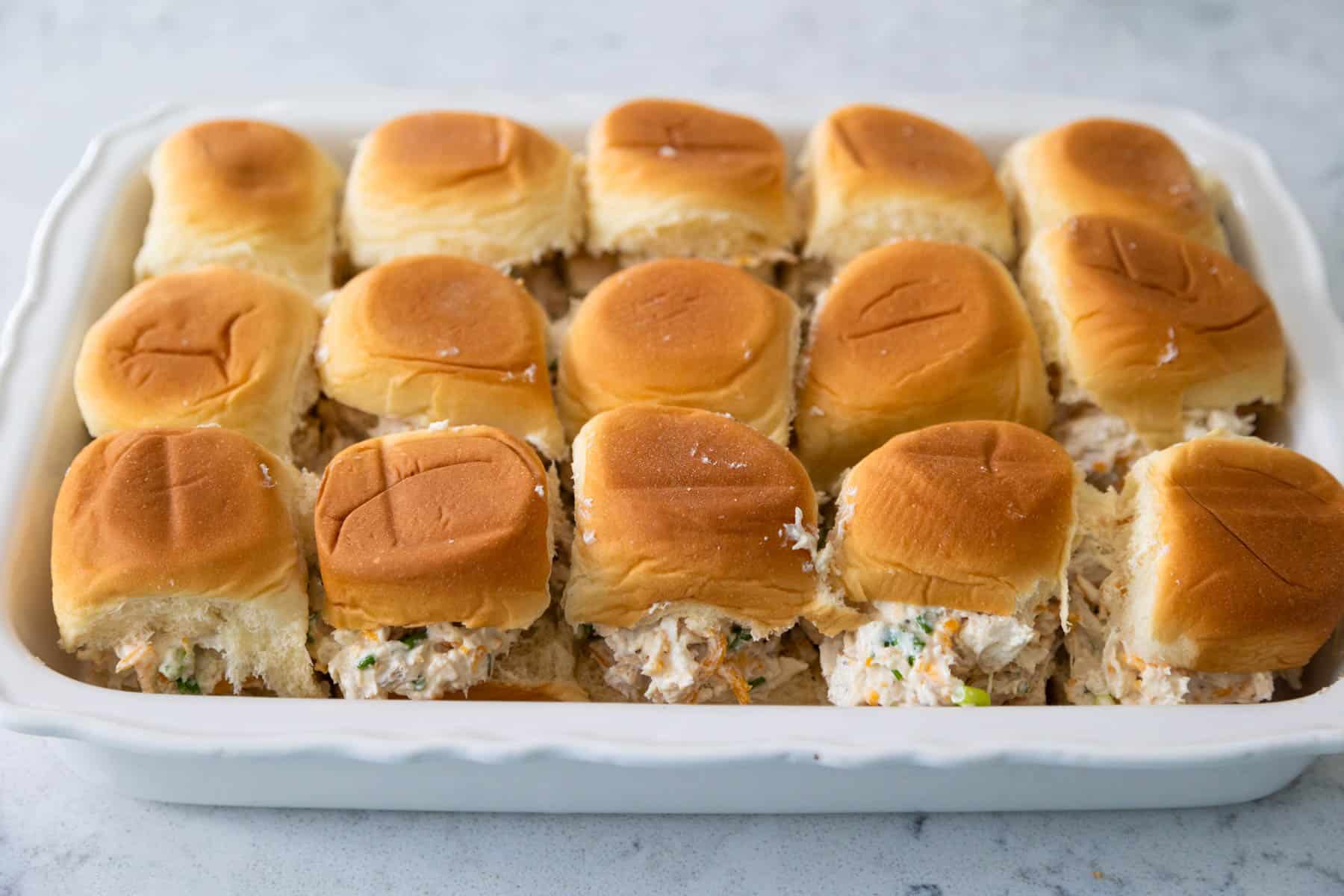 The baking pan has rows of hawaiian buns filled with crack chicken.