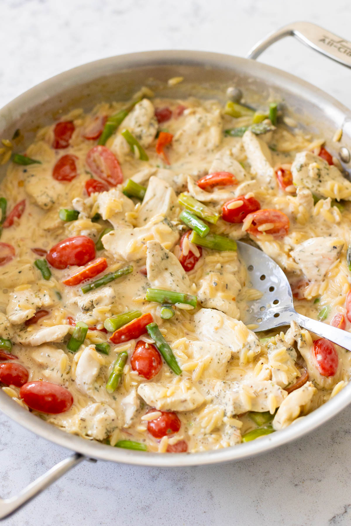The skillet is filled with orzo, chunks of chicken, asparagus and cherry tomatoes, all in a rich and creamy sauce.
