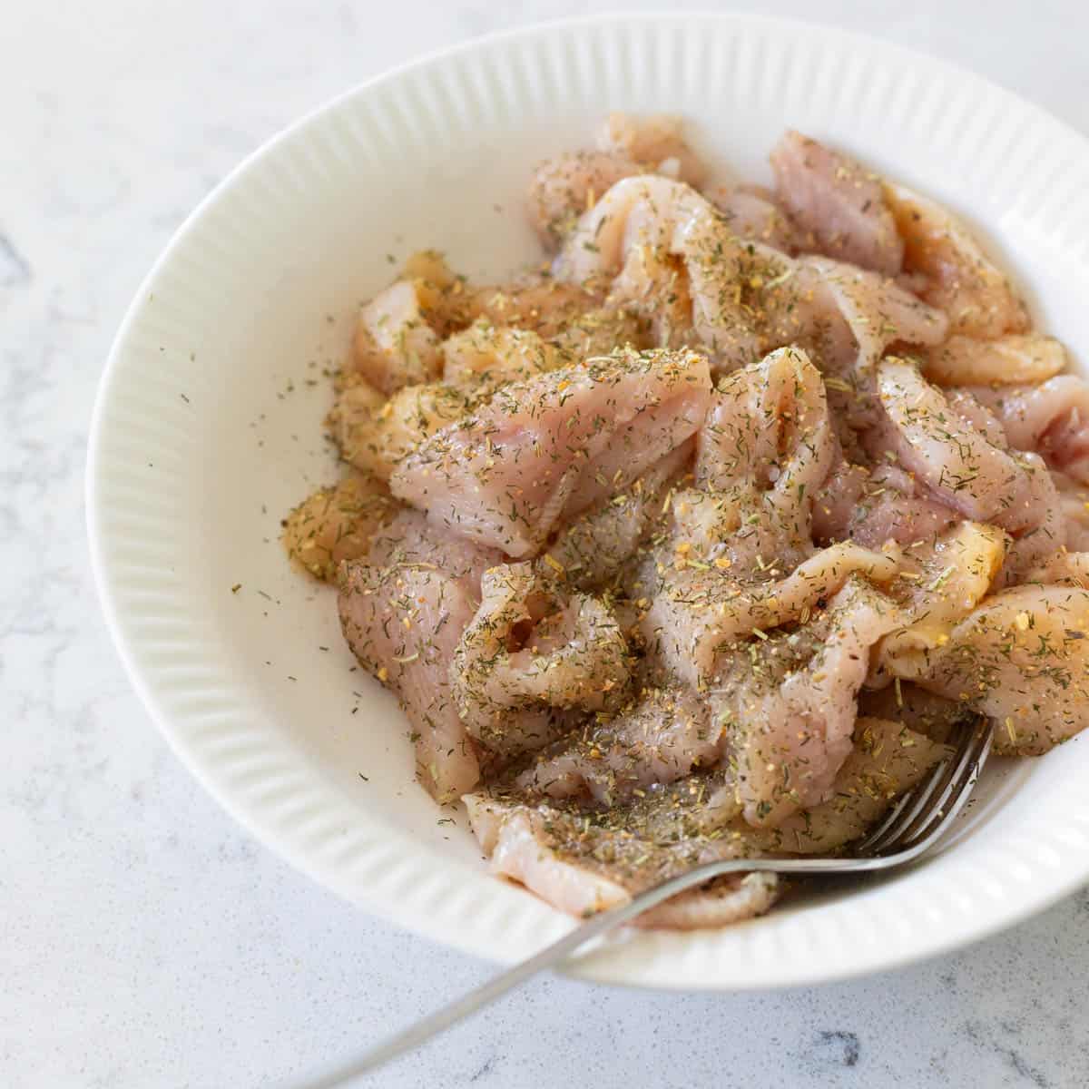 The chicken has been sliced into thin stir-fry sized pieces and seasoned in a bowl.