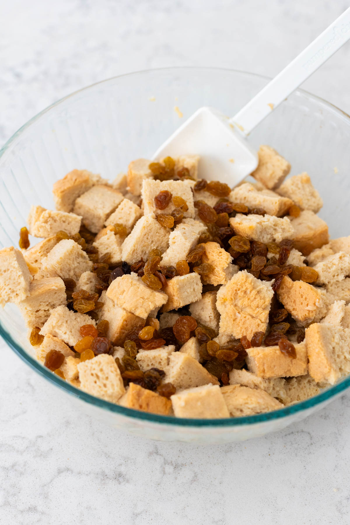 The cubes of French bread and golden raisins are soaking in the egg custard mixture in a large mixing bowl.