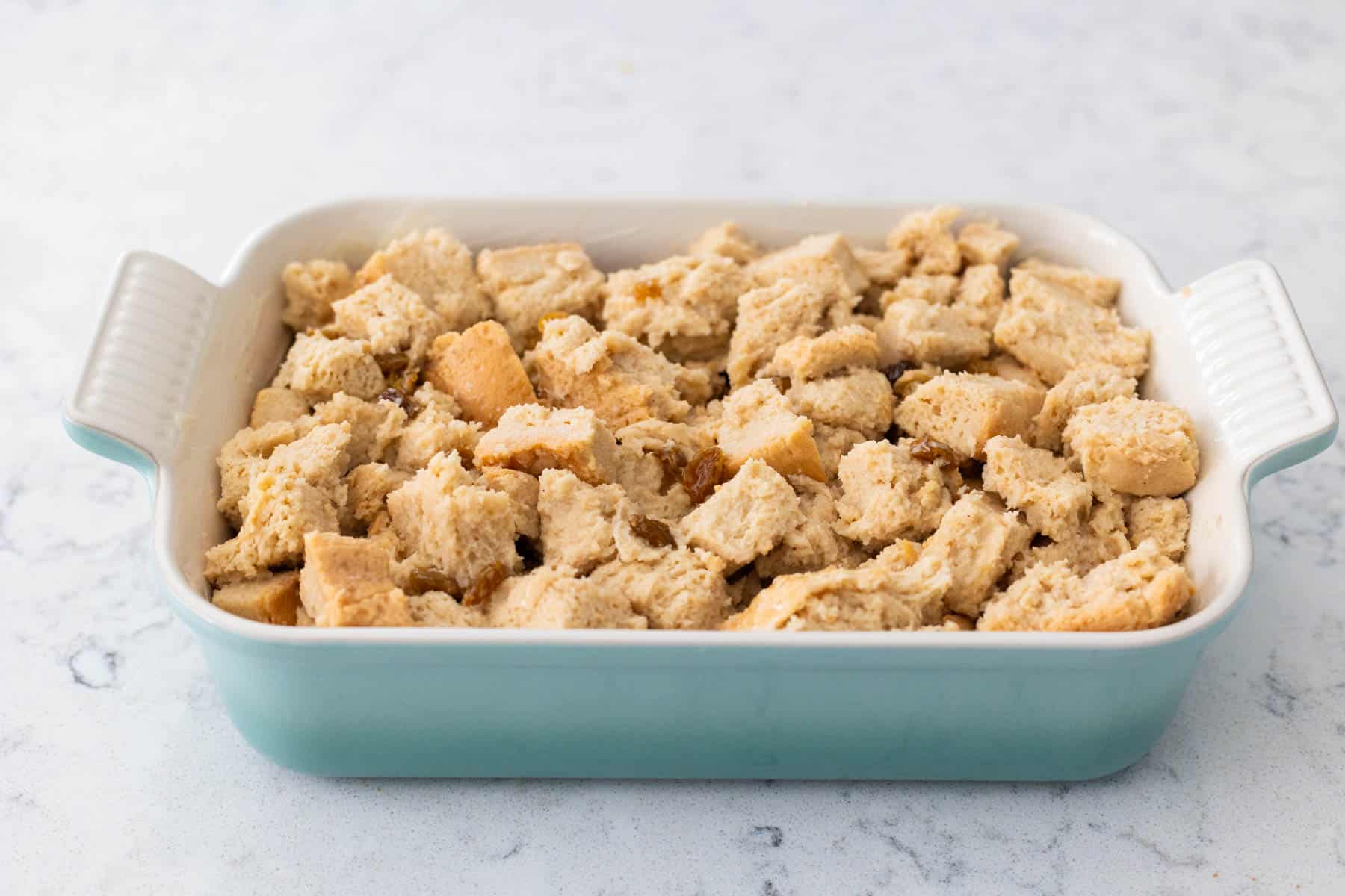 The bread and custard mixture are layered into a blue baking dish.