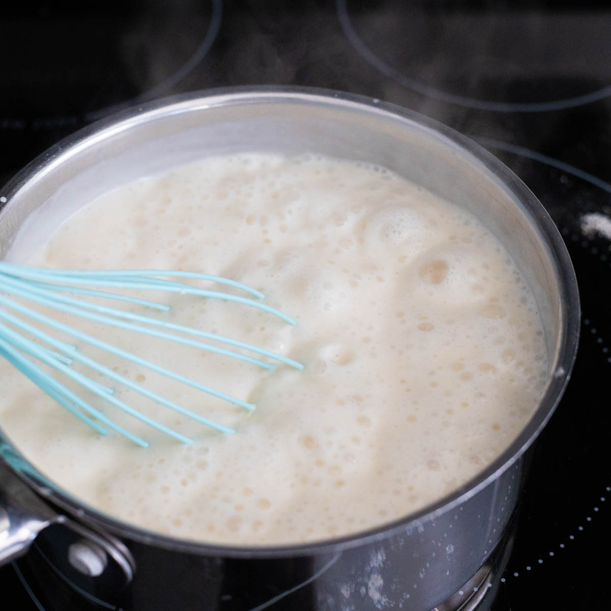 The saucepan of bourbon sauce is at a rolling boil and the whisk is stirring it.