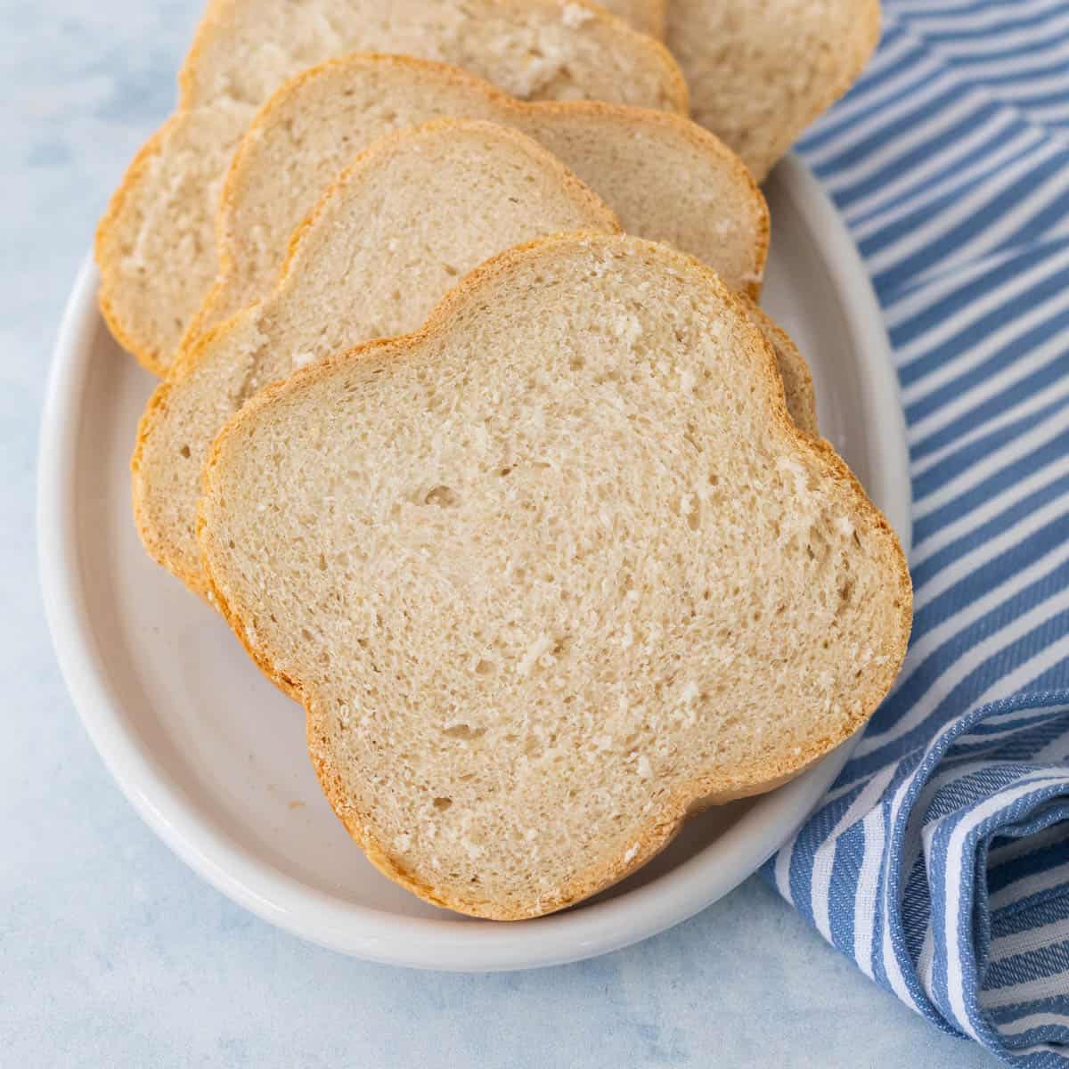 A sliced white bread is on a white platter next to a blue and white striped towel.