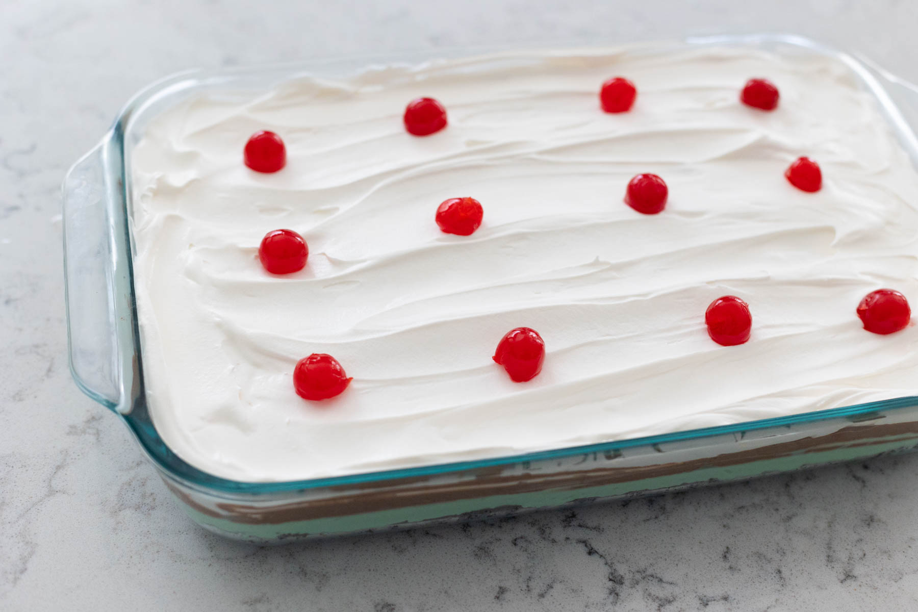 The finished torte has whipped topping frosting and maraschino cherries dotted over the top.