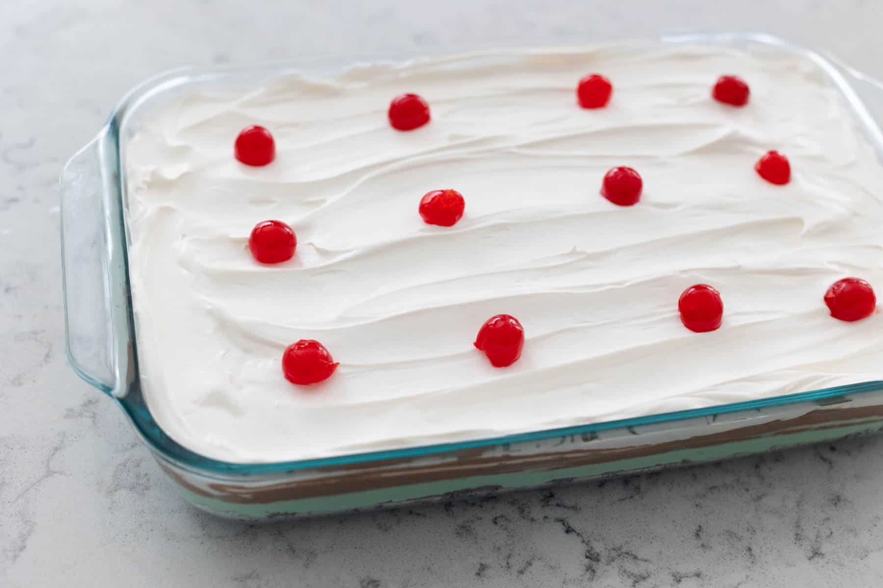 The finished torte has whipped topping frosting and maraschino cherries dotted over the top.