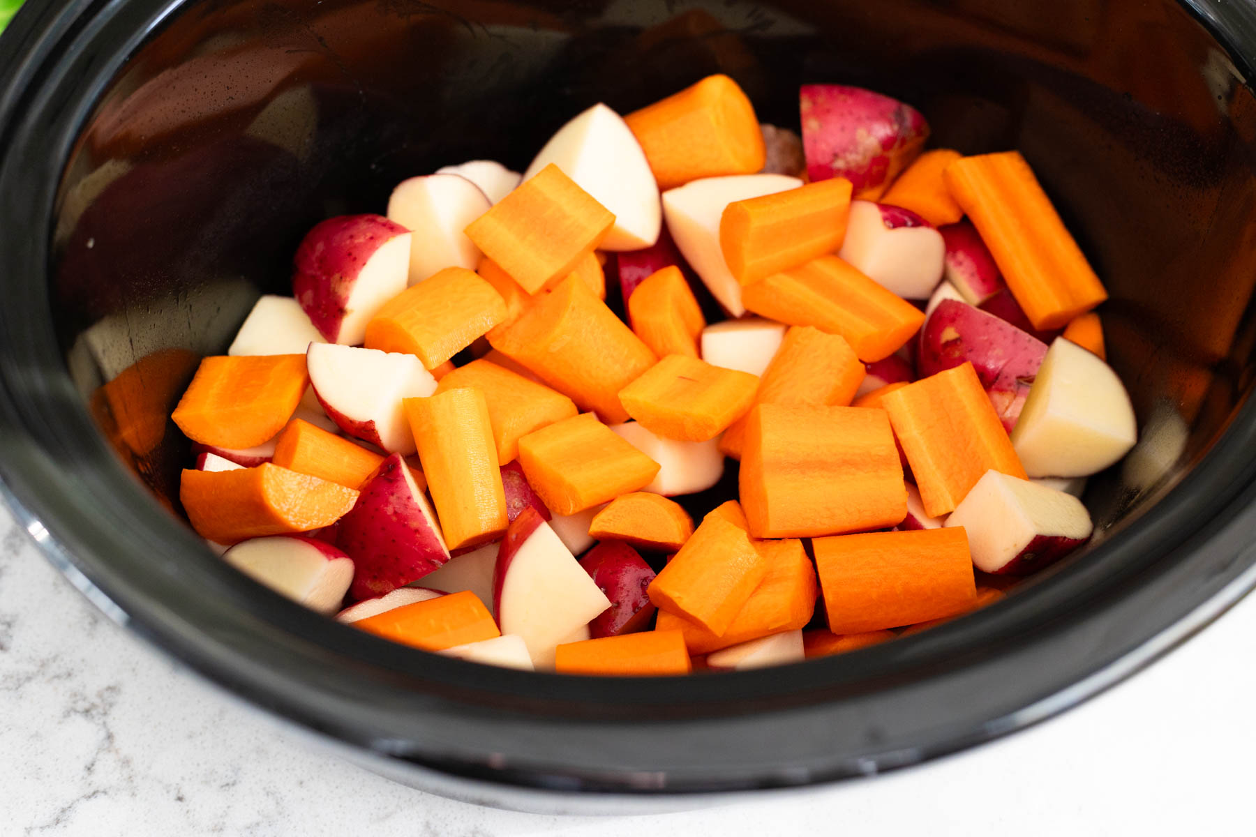 The chopped potatoes and carrots are in the slowcooker pot.