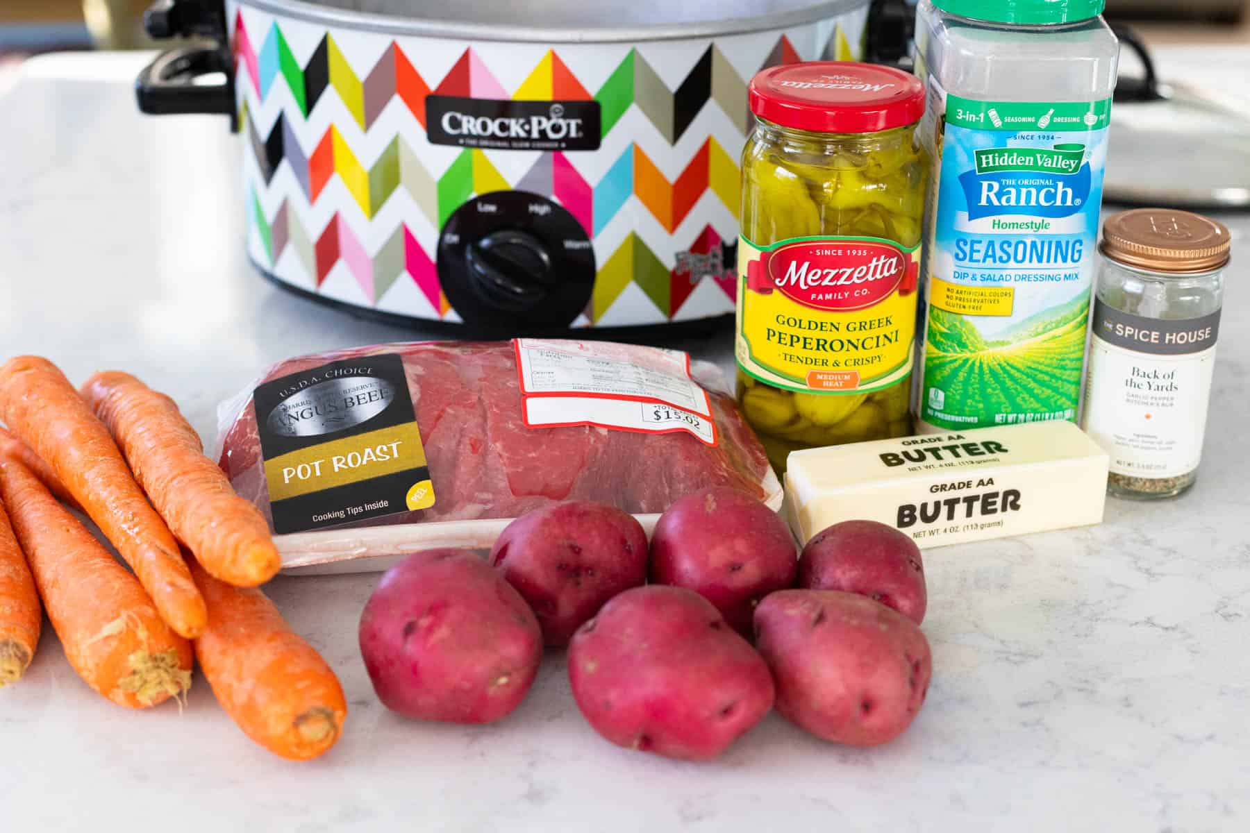 The ingredients to make a mississippi pot roast with potatoes and carrots in the Crock pot are on the kitchen counter.