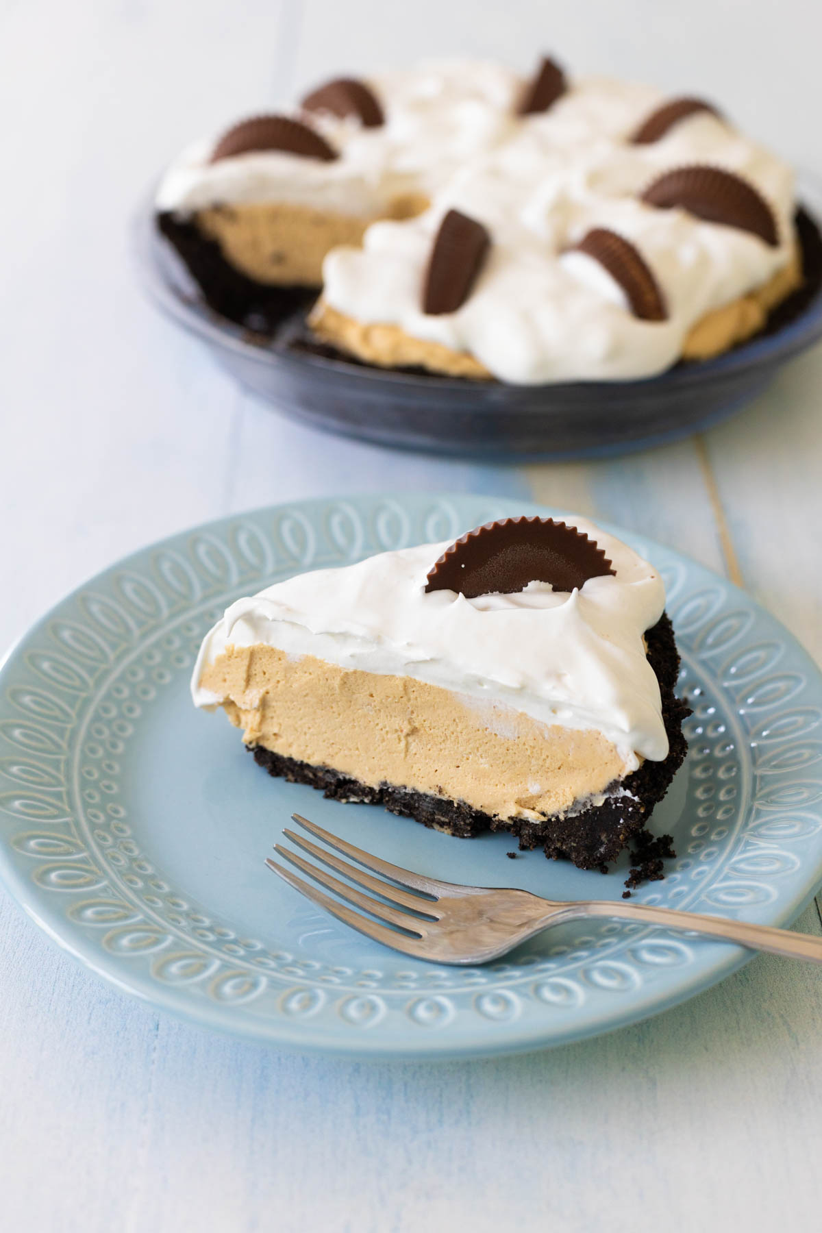 A slice of peanut butter pie is on a blue plate next to the full pie plate.