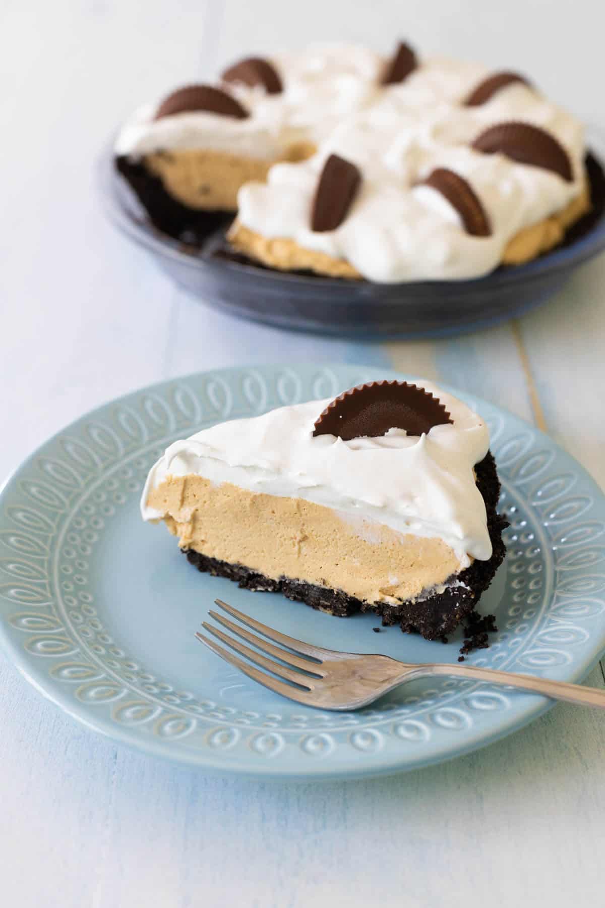 A slice of peanut butter pie is on a blue plate next to the full pie plate.