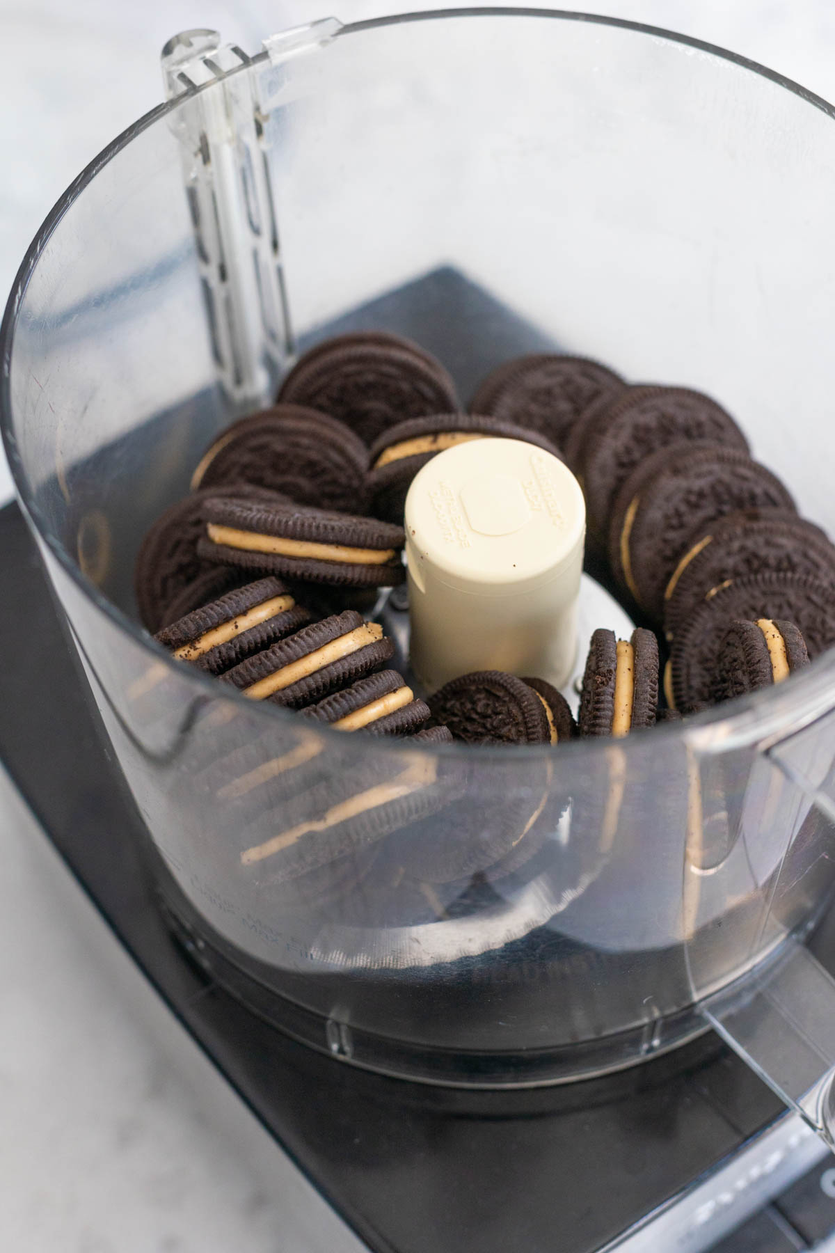 The food processor bowl is filled with peanut butter Oreo cookies about to be crushed.
