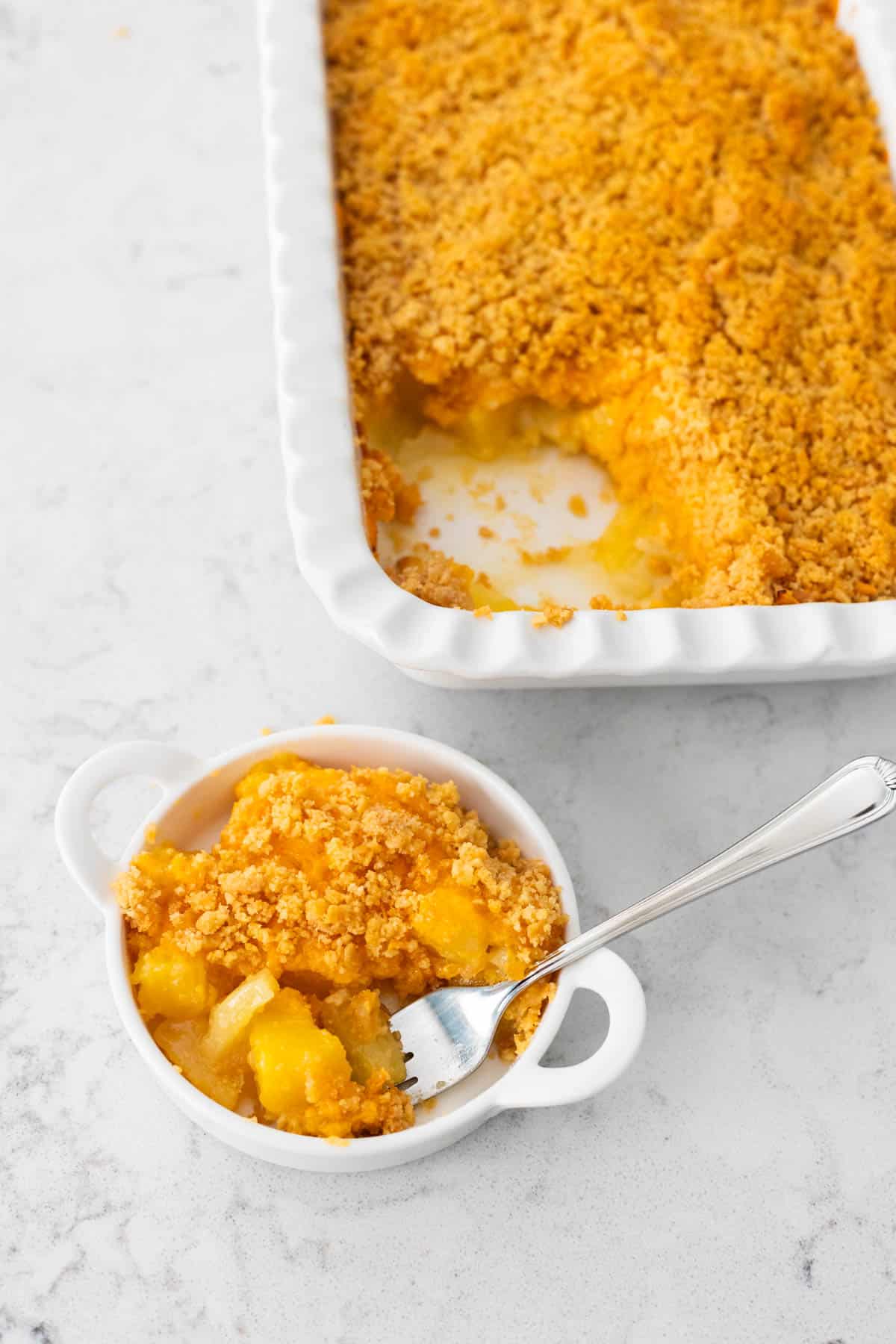 The baking pan of casserole sits next to a small bowl with one serving and a fork.