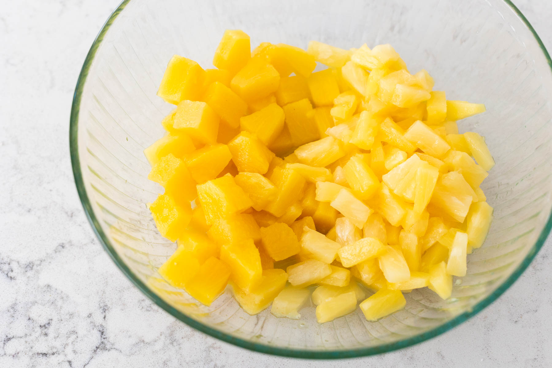 A mixing bowl is filled with canned pineapple. The pineapple chunks are on the left, the pineapple tidbits are on the right.