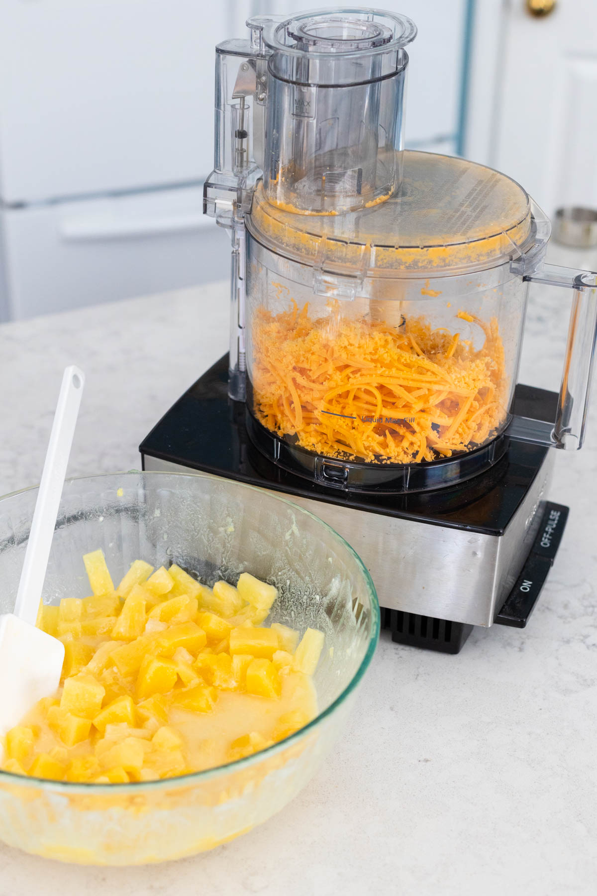 The food processor on the counter has just finished shredding cheddar cheese.