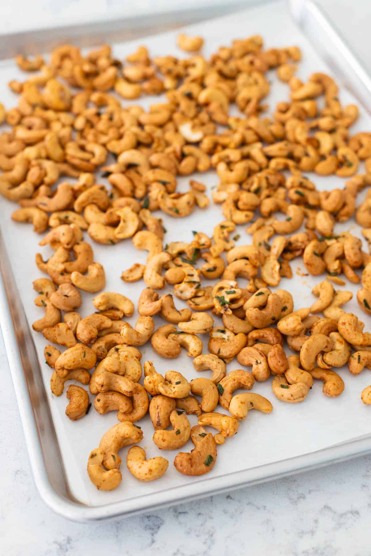 The seasoned cashews are on a large baking sheet lined with parchment paper.