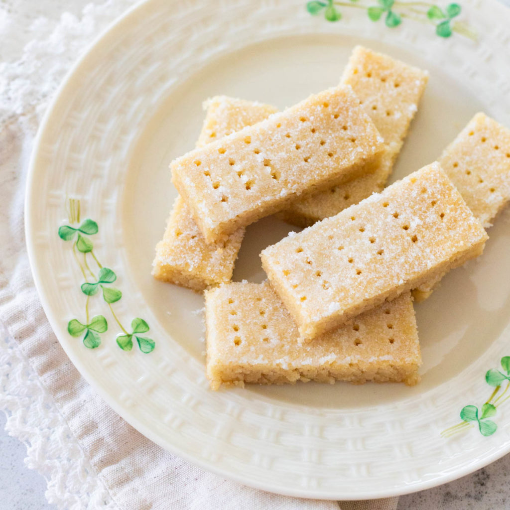 A plate with shamrocks on it has a stack of homemade Irish shortbread cookies cut into rectangles.