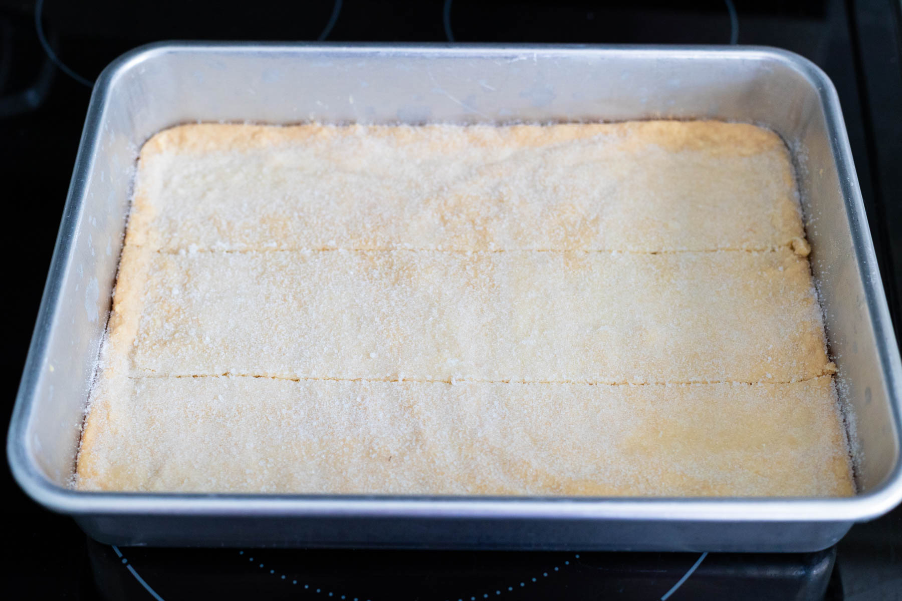 The pan of baked shortbread has two slices dividing it lengthwise into thirds.