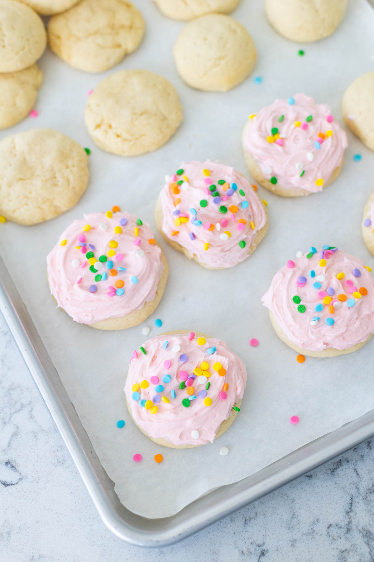 A baking sheet of sugar cookies shows half of them frosted with sprinkles and half of them plain.