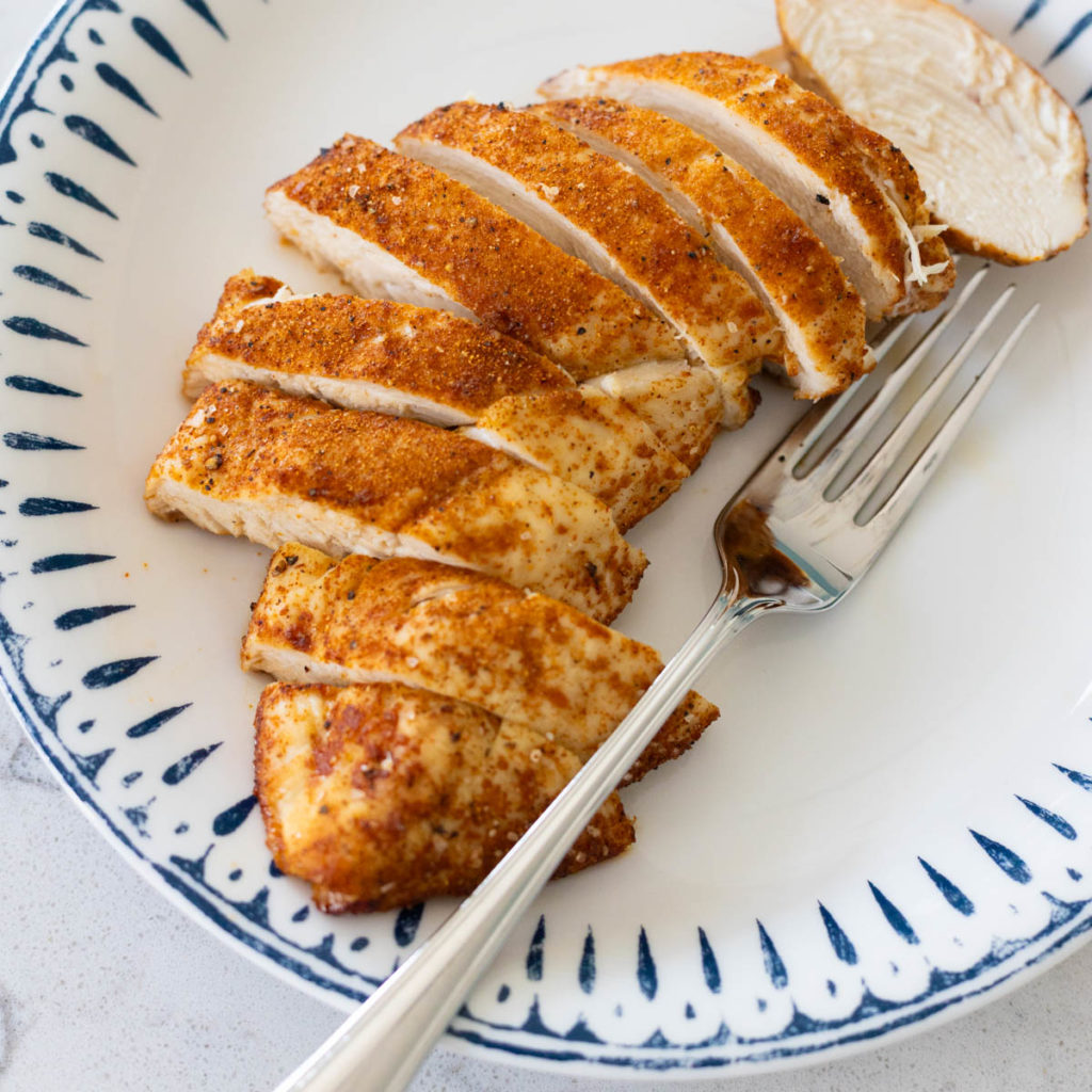 The dry rub has seasoned a chicken breast which has been cooked and sliced on a plate.