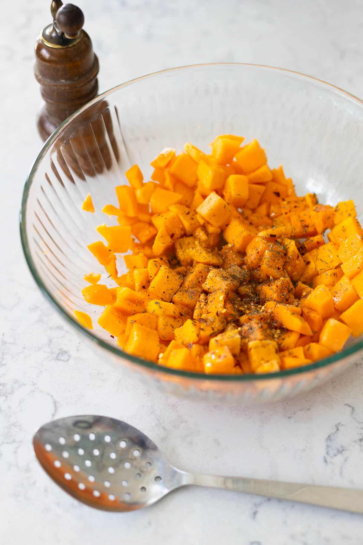 The butternut squash is being seasoned in a large mixing bowl.