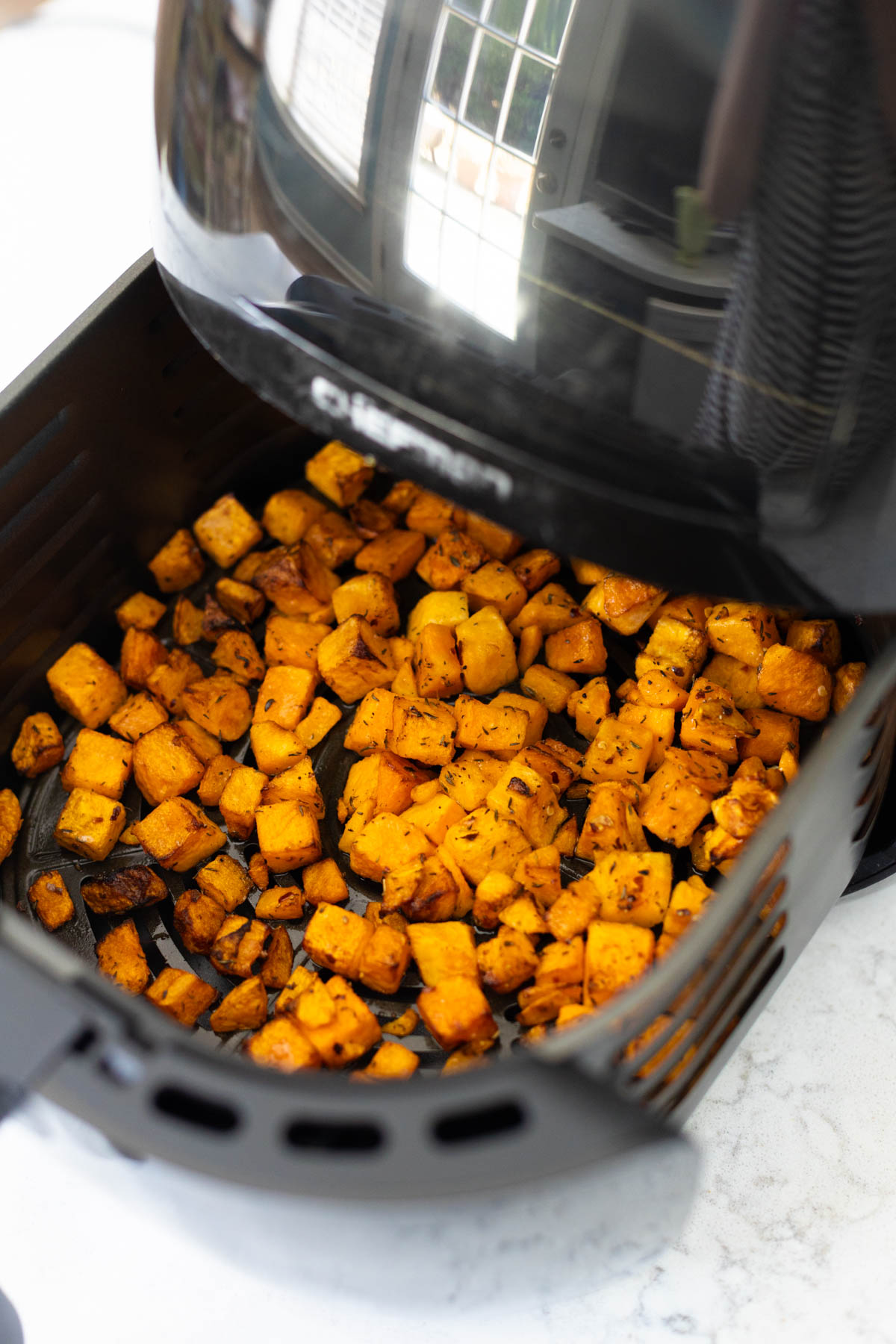 The air fryer basket is open and shows the butternut squash inside.