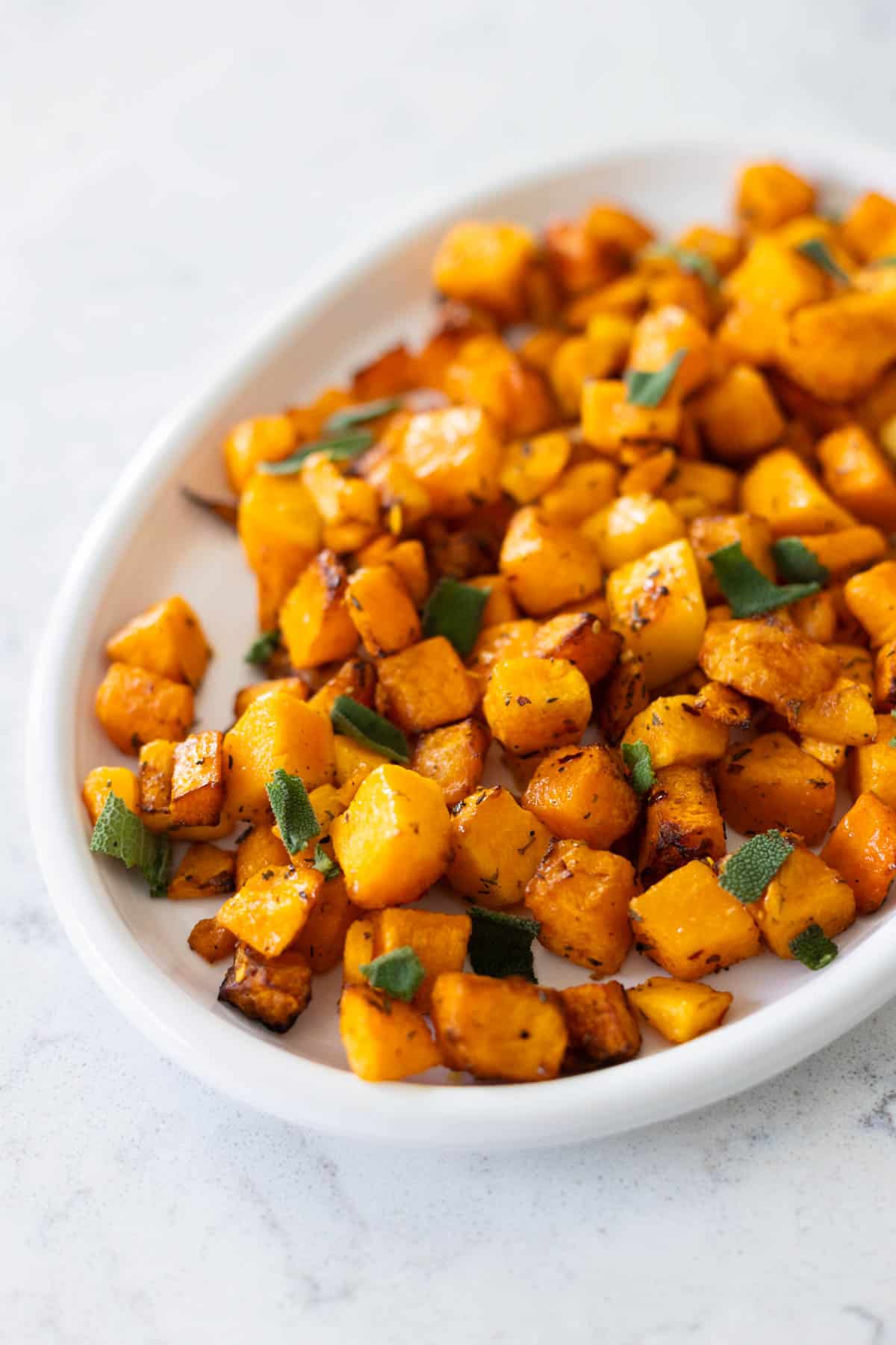 The white platter is filled with butternut squash and fresh sage leaves.