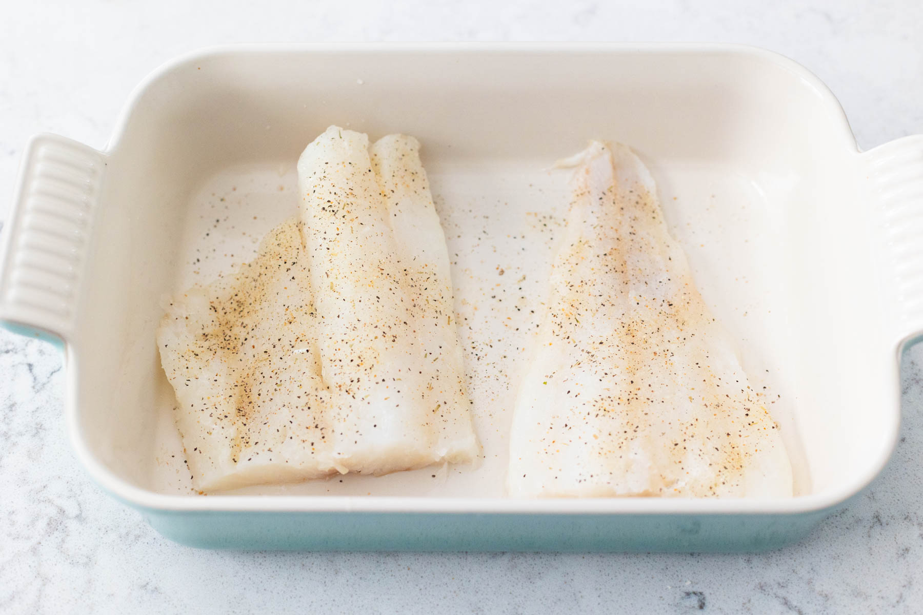 The cod filets are in a baking dish and seasoned.