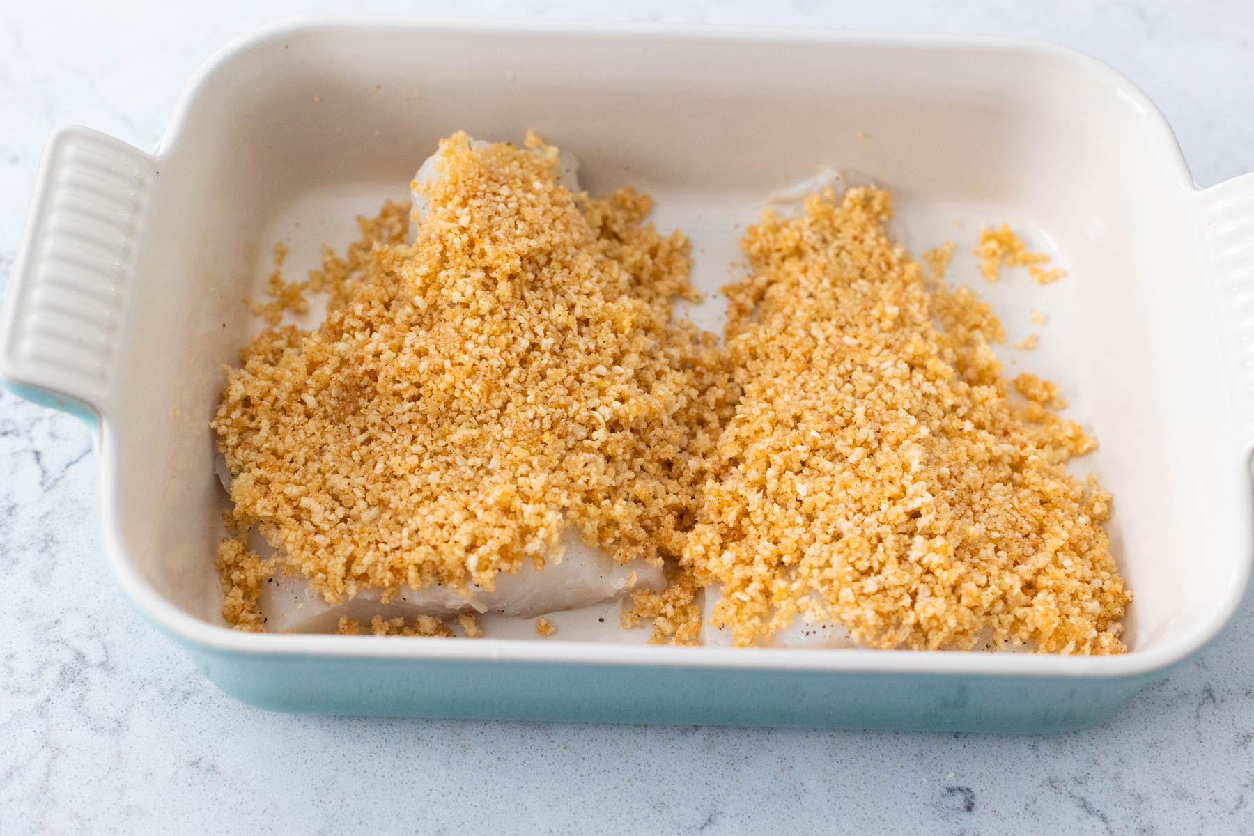 The fish filets have the breadcrumb mixture spread on top.