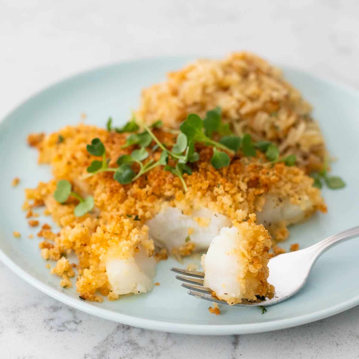 The breaded fish is on a blue plate with a scoop of rice pilaf.