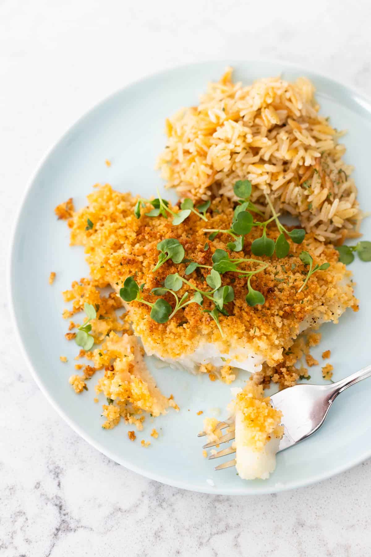 The crispy cod filet is on a blue plate with a scoop of rice pilaf.