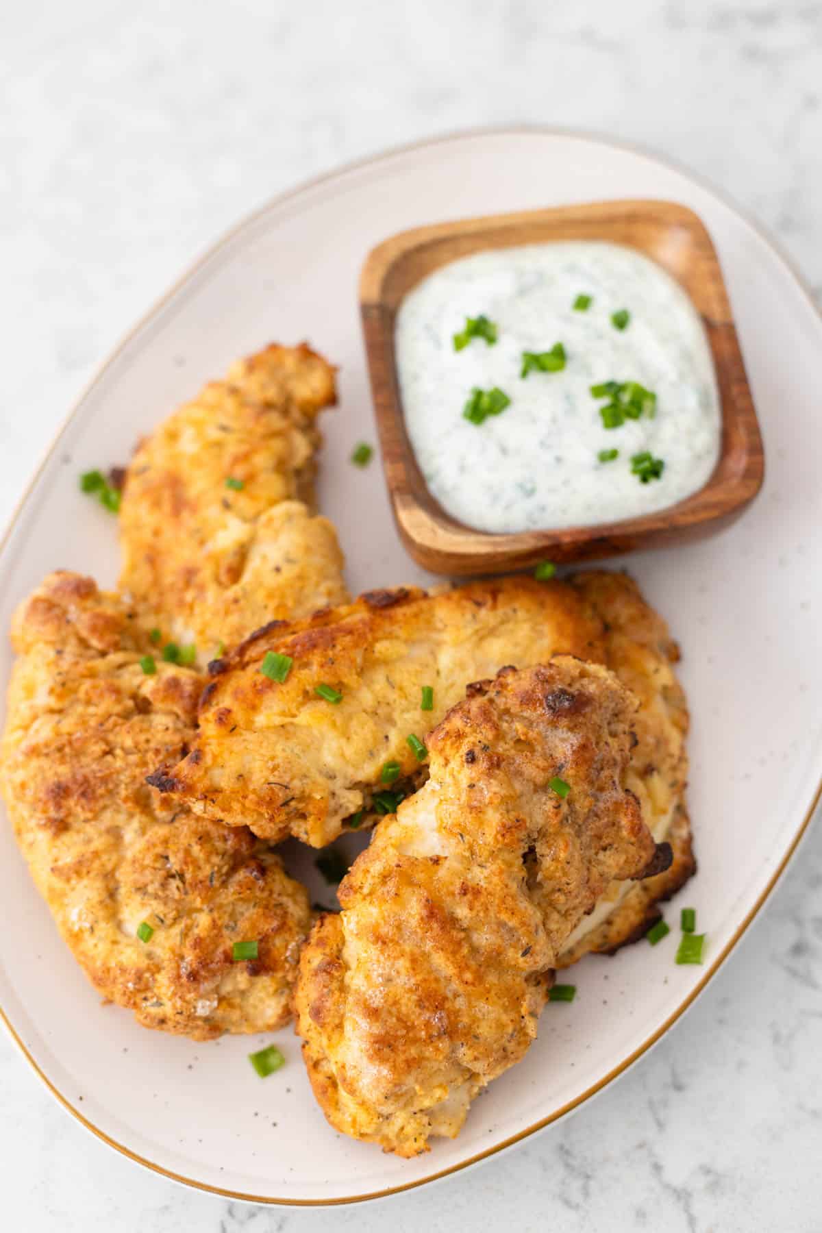 The breaded fried chicken tenders are on a platter with a cup of ranch dipping sauce.