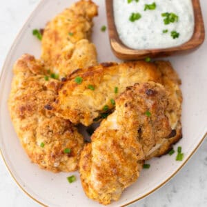 A platter of buttermilk fried chicken tenderloins with a cup of ranch.