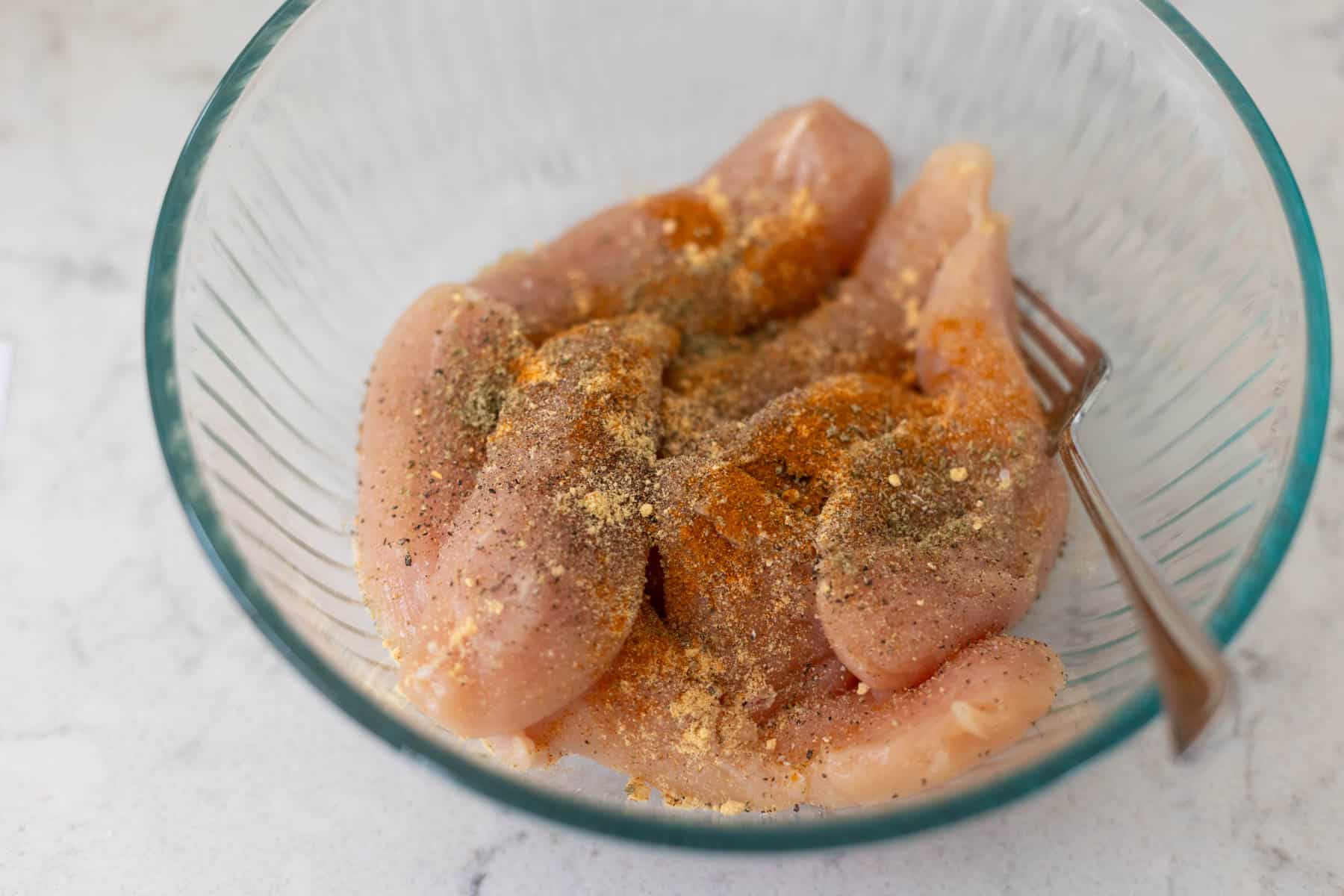 The chicken has been seasoned in a mixing bowl.