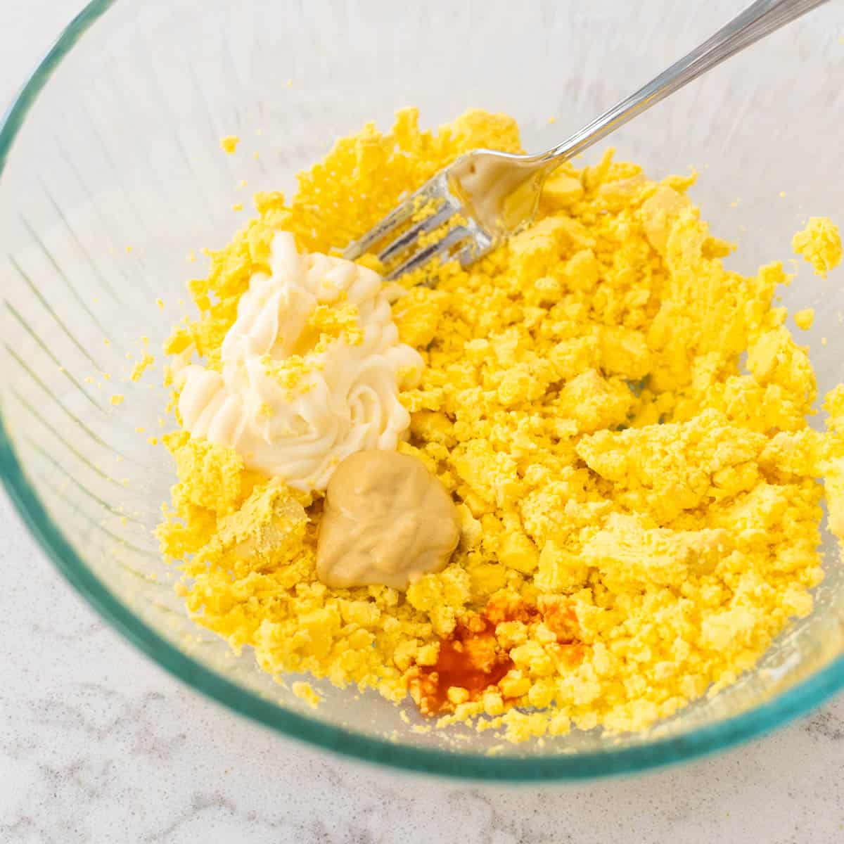 The yolks have been mashed in a mixing bowl with a fork. The remaining ingredients are about to be mixed in.