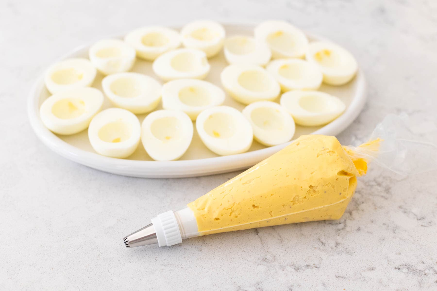 The piping bag has been filled with the deviled egg filling and is sitting in front of the empty egg whites.