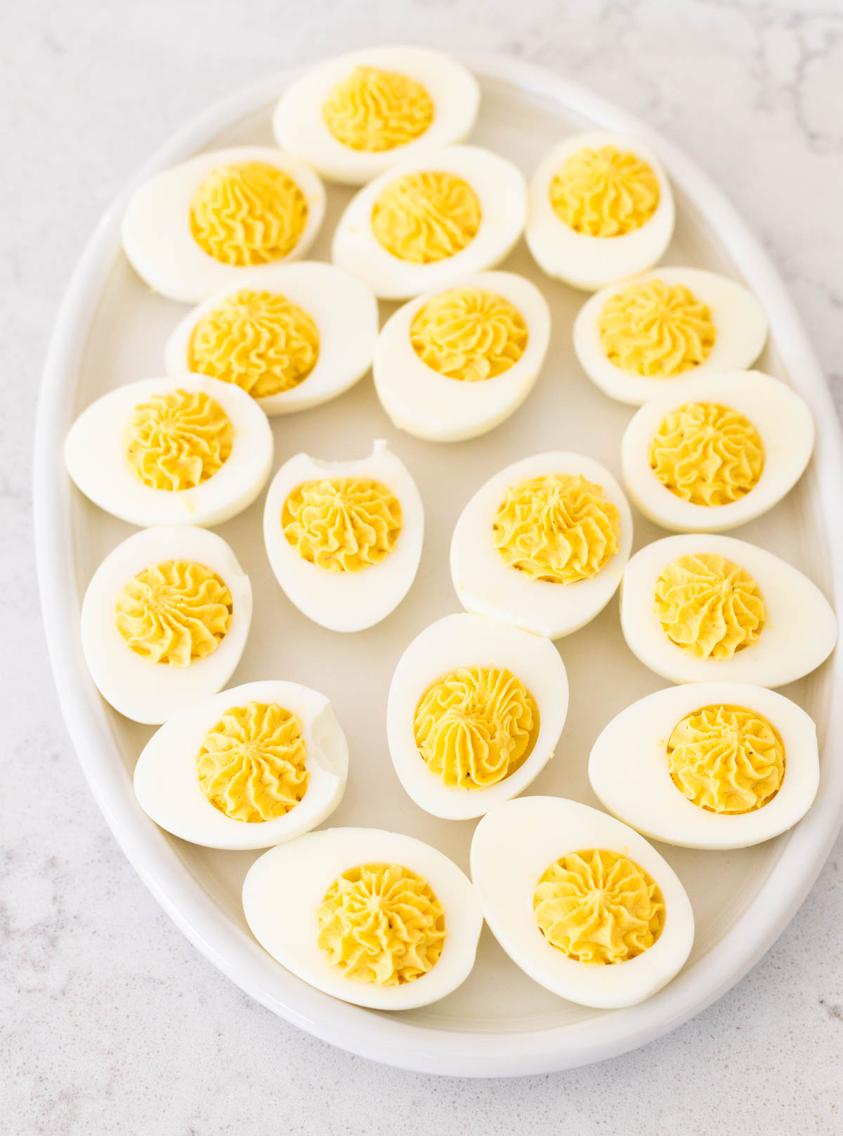 The egg whites have had the yolk filling piped into them and are on a white platter.