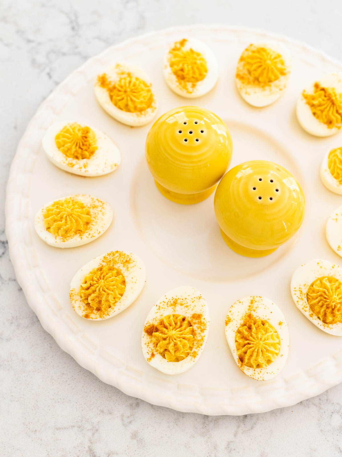 The egg platter is filled with deviled eggs and has a pair of yellow salt and pepper shakers in the middle.