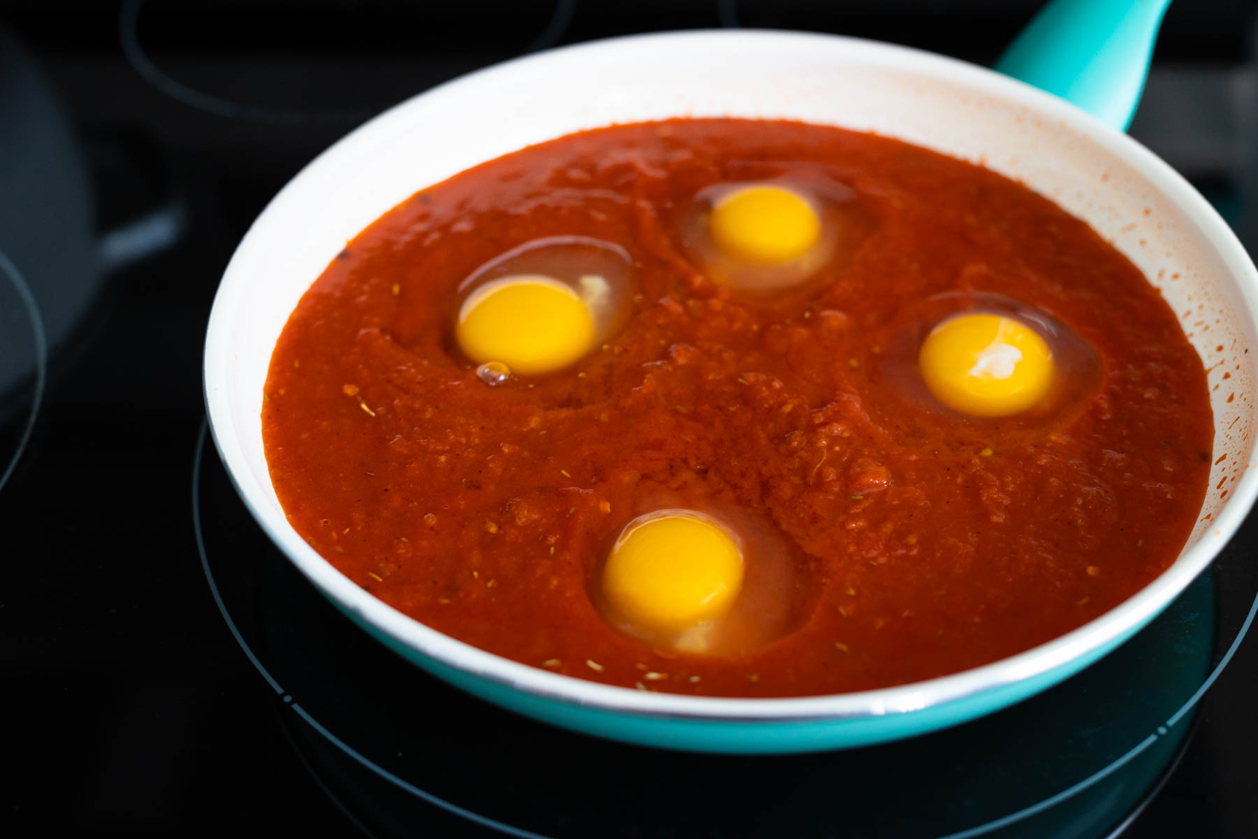 the four eggs have been added to the tomato sauce in the skillet.