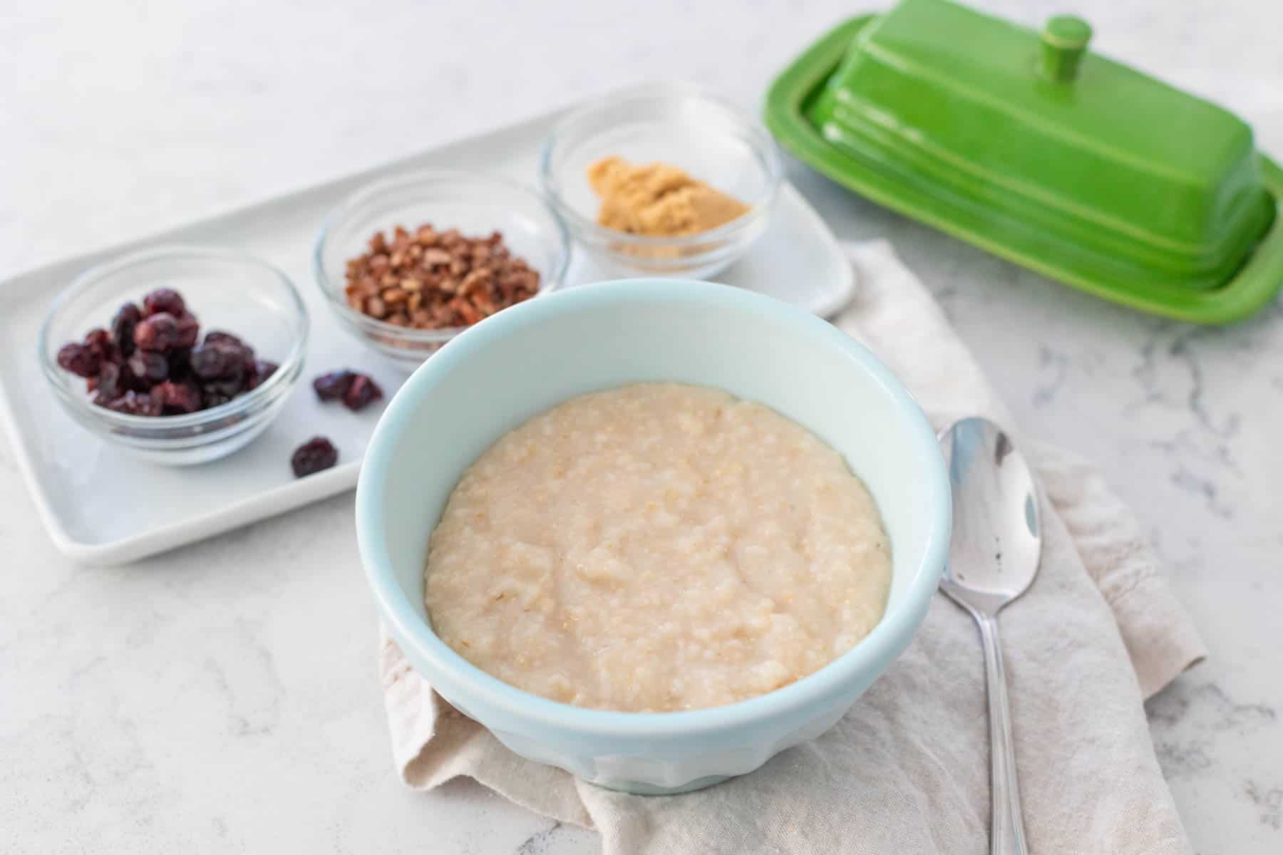 The plain bowl of Irish oatmeal sits next to a tray of toppings including small bowls of dried fruit and nuts.