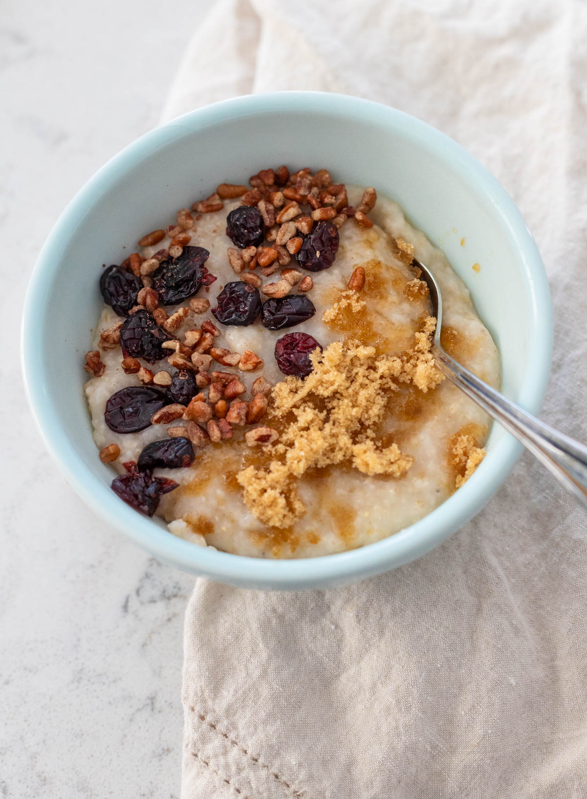 A bowl of creamy oatmeal with craisins, chopped pecans, and brown sugar on top.