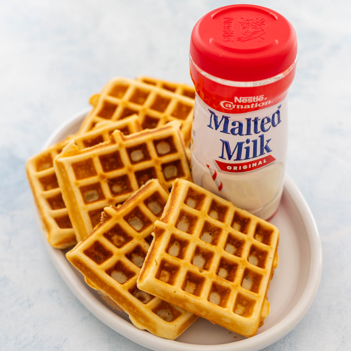A platter of malted waffles has a bottle of Carnation Malted Milk on the side.
