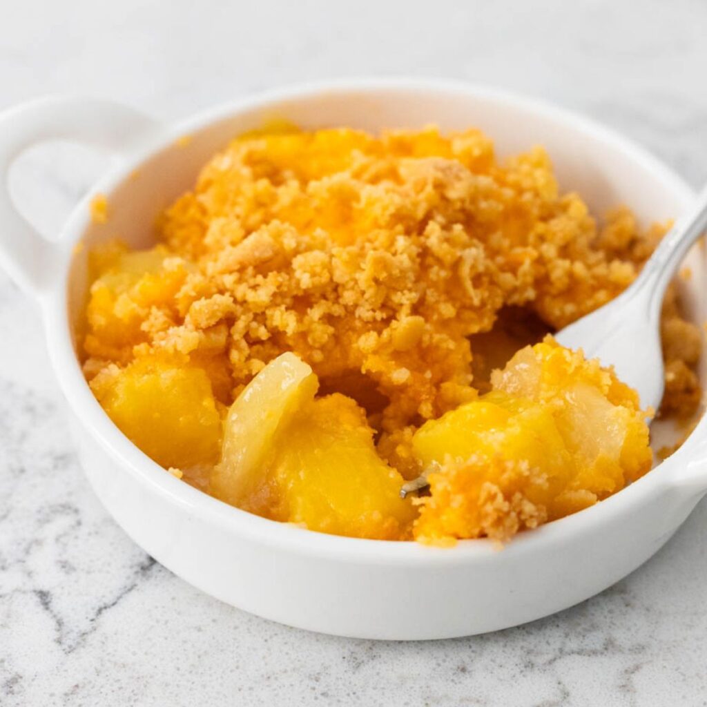 A small white dish has a serving of pineapple cheese casserole with cracker crumb topping.