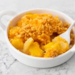 A small white dish has a serving of pineapple cheese casserole with cracker crumb topping.