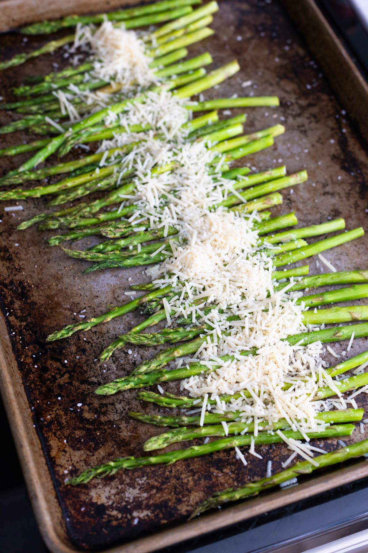 The shredded parmesan has been sprinkled over the asparagus on the baking sheet.