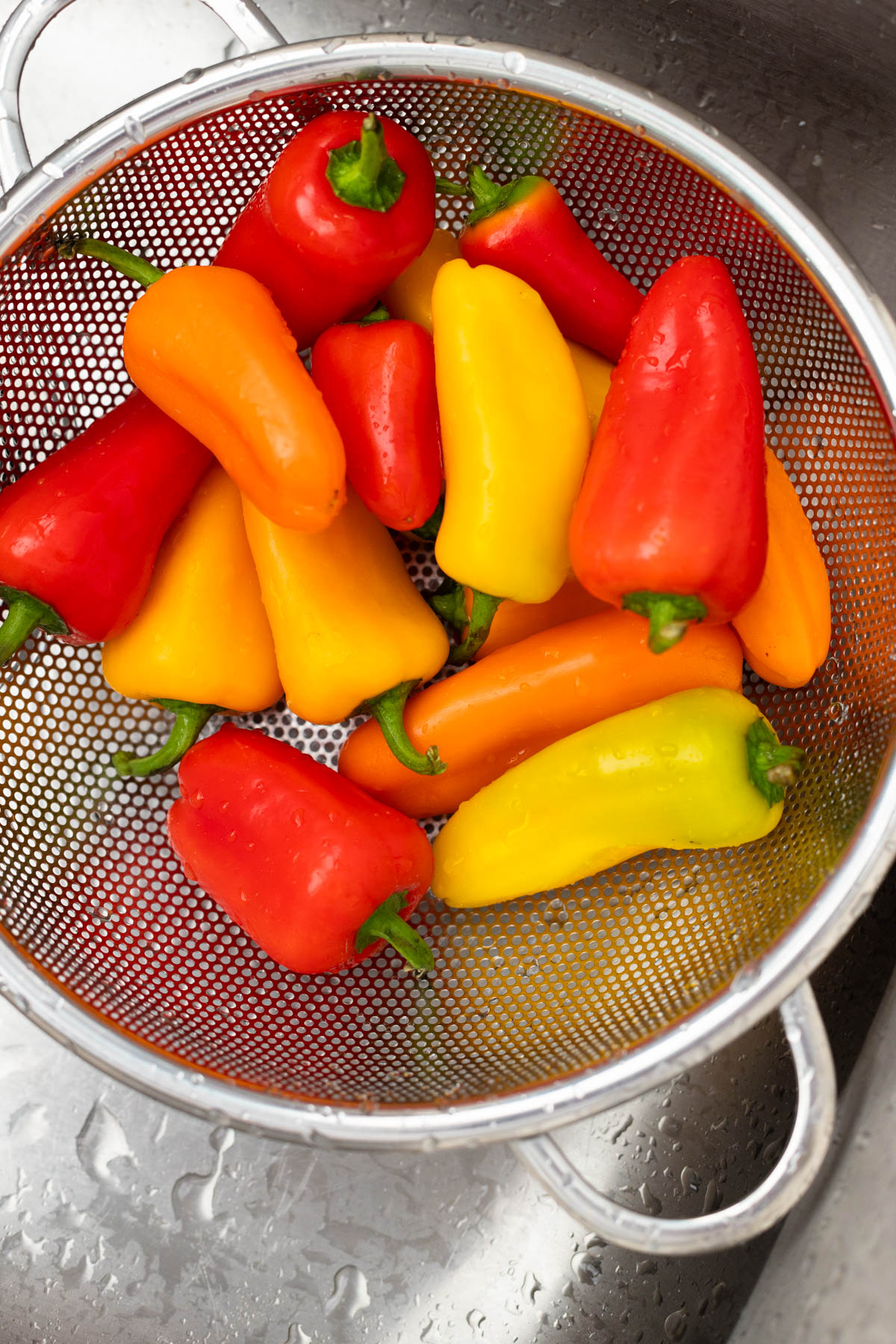 The sweet peppers are in a colander in the sink.
