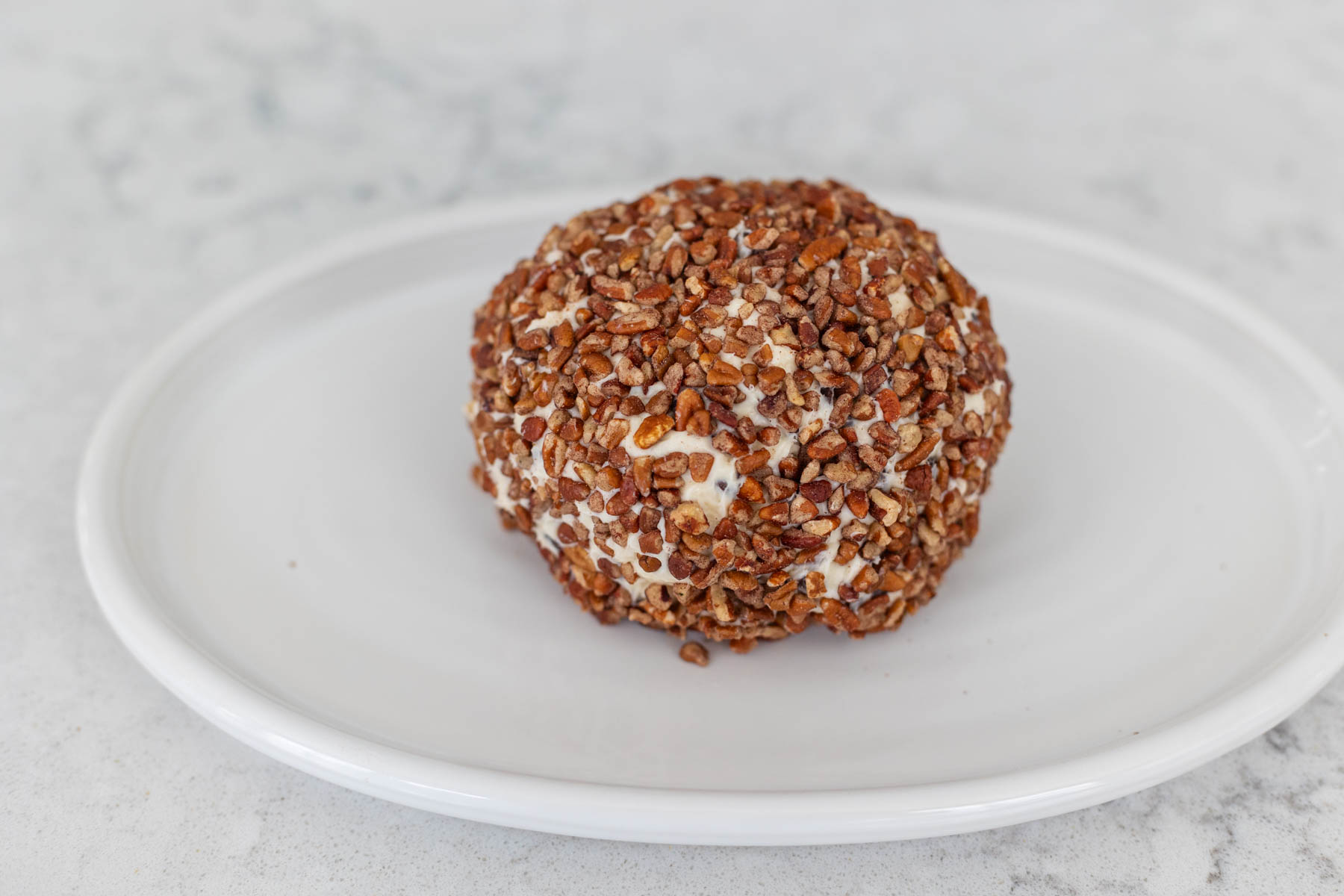 The coated sweet cheese ball is sitting on a white platter ready for the fridge.