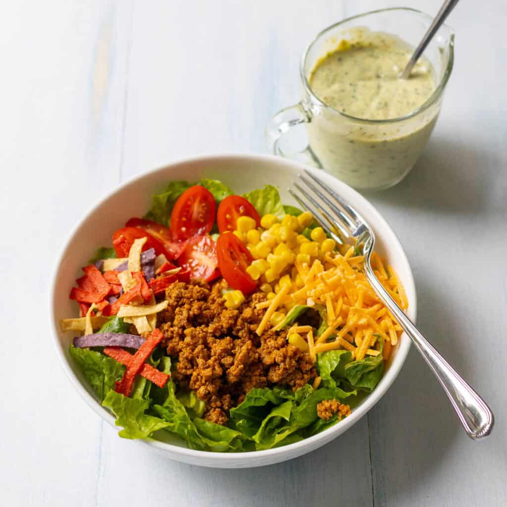 A taco salad in a bowl next to a pitcher of dressing.