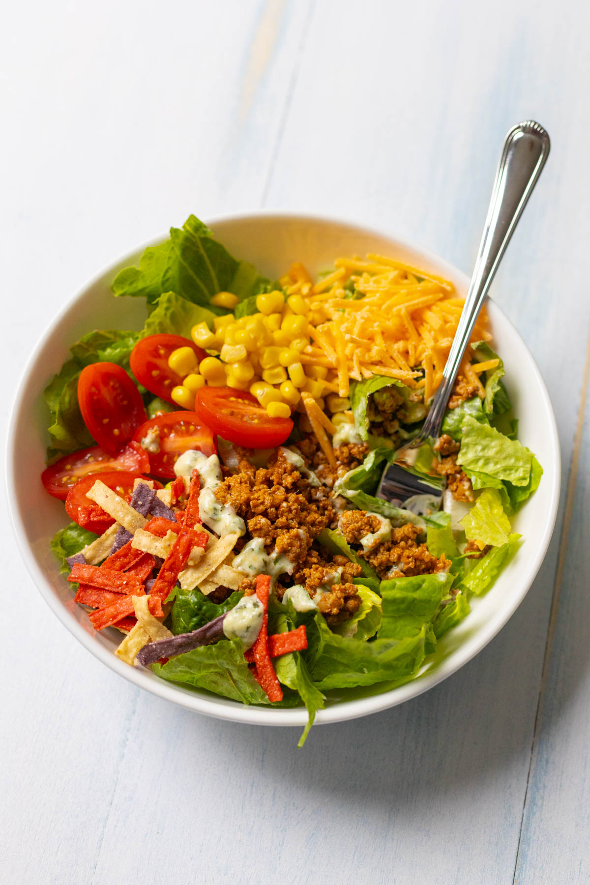 A fresh taco salad with lettuce and fresh tomatoes has ground turkey on top.